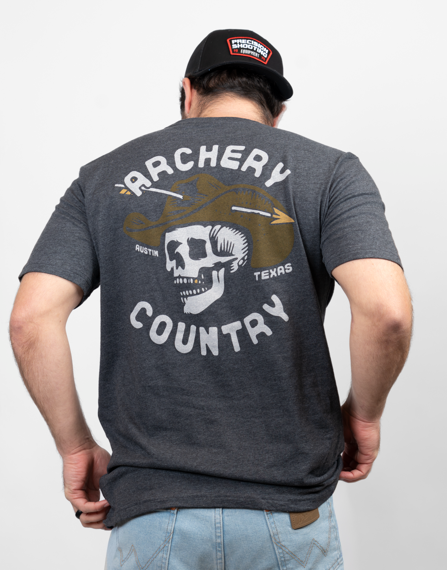 Rear view of man wearing charcoal tee with graphic of  a skull wearing a cowboy hat with an arrow through it with text "ARCHERY COUNTRY AUSTIN TEXAS"